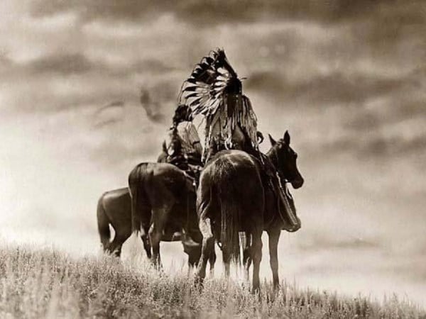 Native american men riding horses in field. 