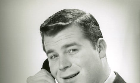 A black and white photo of a man talking on the phone. He appears to be overcoming his shyness.