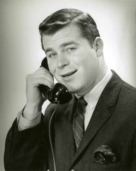 A black and white photo of a man talking on the phone. He appears to be overcoming his shyness.