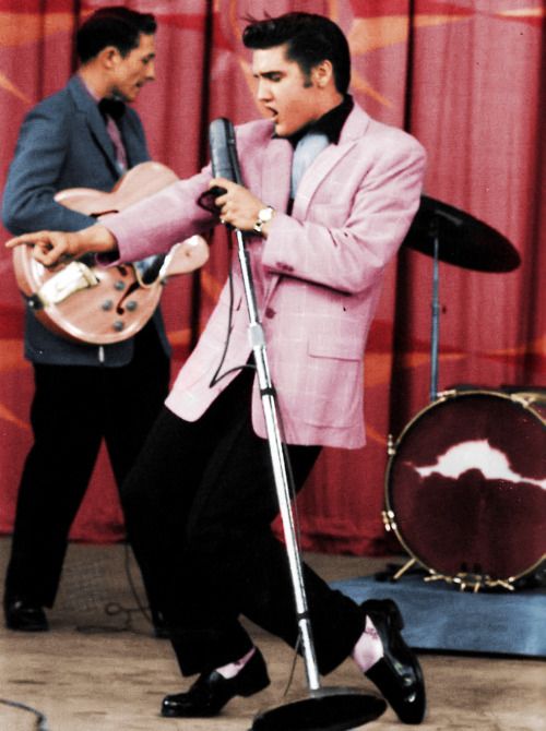 Elvis wearing pink blazer & performing on stage.