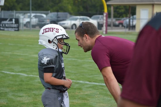 A coach giving instructions to a little footballer in ground.