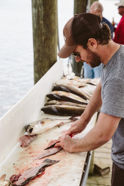 Man fileting fish on dock. 