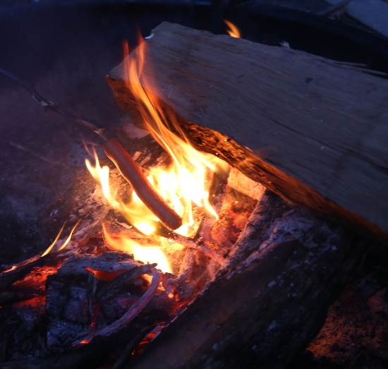 Hot dog cooking on stick over fire.