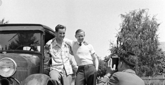 Three friends standing in front of a car with a camera, highlighting the importance of keeping in touch.