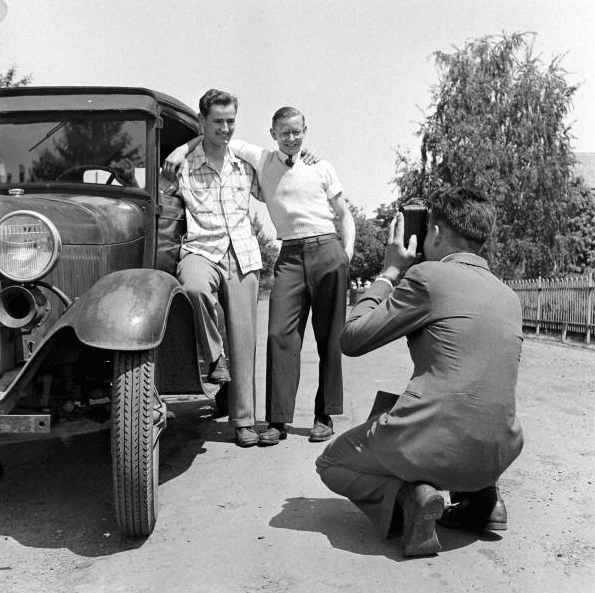 Three friends standing in front of a car with a camera, highlighting the importance of keeping in touch.