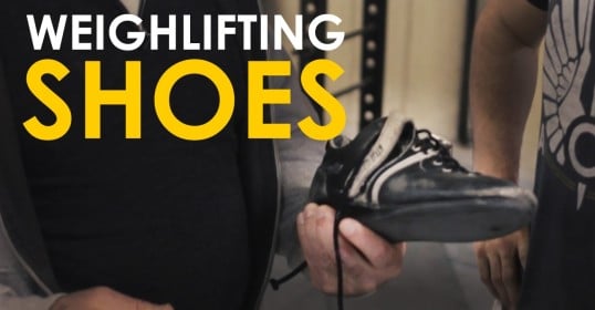 A man is holding a pair of weightlifting shoes in a video.