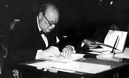 Winston Churchill sitting at desk and writing with fountain pen. 