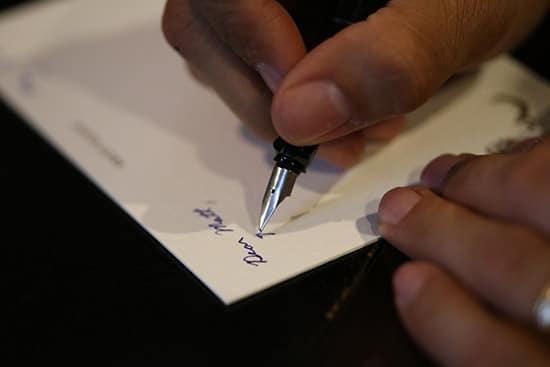 A man using fountain pen to write at the corner of paper. 