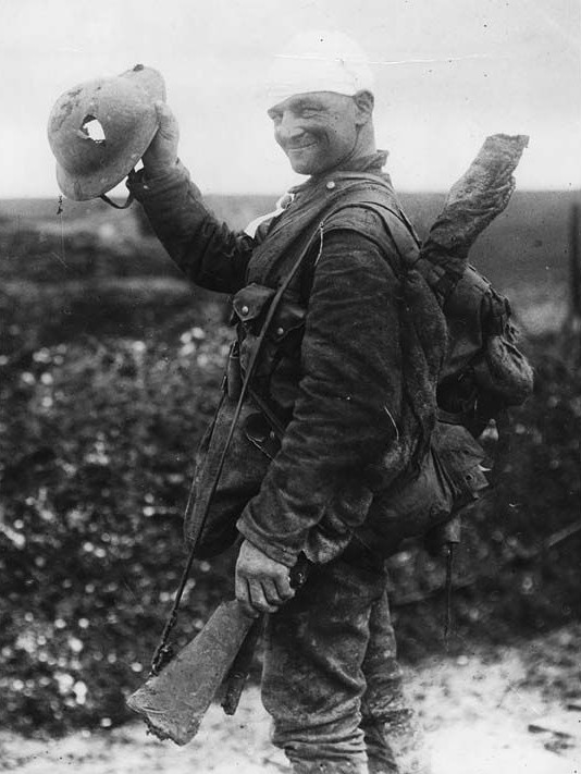 wwii soldier holding up helmet with bullet hole through it
