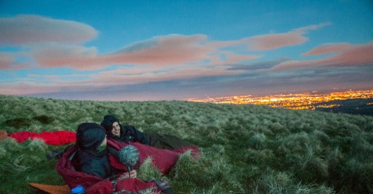 Two people getting out there on a grassy hill at night.