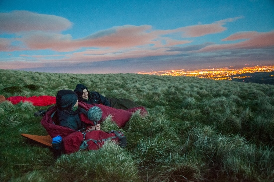 Two people getting out there on a grassy hill at night.