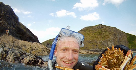 A man getting out there in the water, holding up a crab.