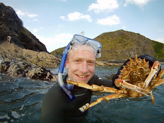 A man getting out there in the water, holding up a crab.