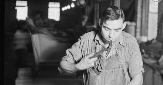 An old black and white photo of a man repairing furniture in a workshop.