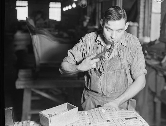 An old black and white photo of a man repairing furniture in a workshop.