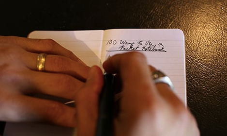 A person using a pen in a pocket notebook.