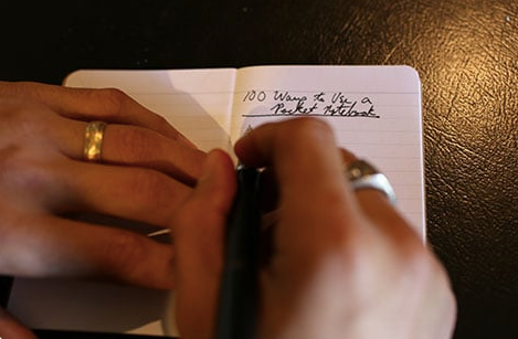 A person using a pen in a pocket notebook.