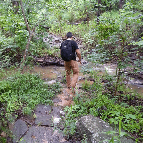 Man hiking rucking over muddy river.