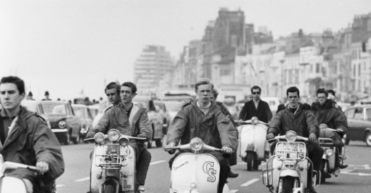 A group of men riding scooters down a street.