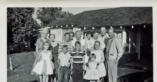 A black and white photo of a family posing in front of their home.