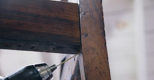A person is using a drill to repair a common wooden chair.