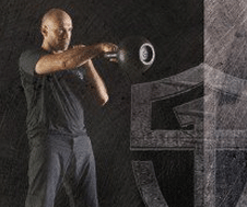 A man is showcasing his strength by holding a kettlebell in front of a black background, demonstrating his expertise in Kettlebell Training.