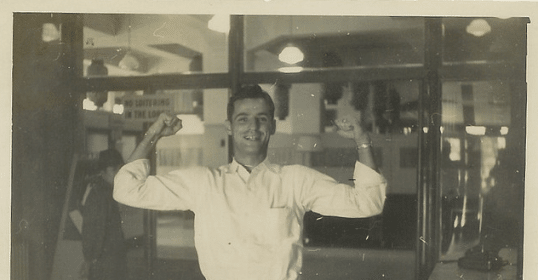 A confident man is flexing his arms in front of a window.