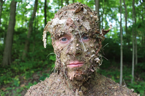 Man face covered with forest debris natural camouflage.