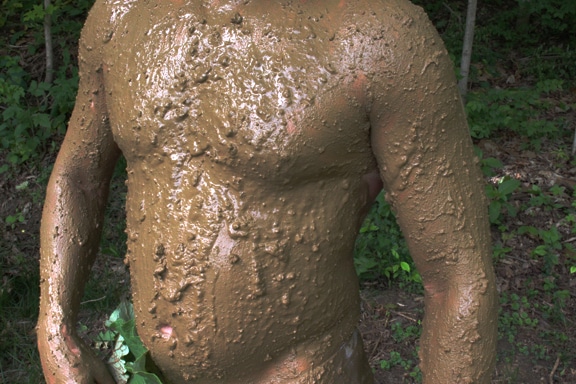 Man covered in mud for camouflaging.