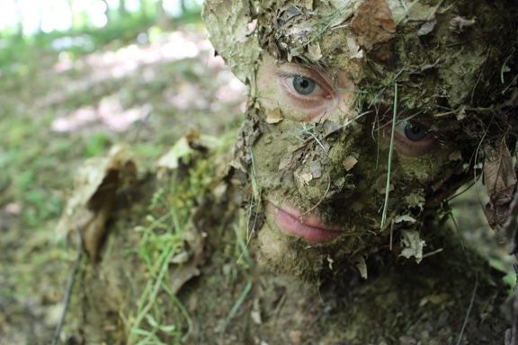 Men face camouflage with mud and leaves.