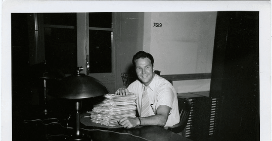 A man sitting at a desk with a stack of papers, paying back student loans.
