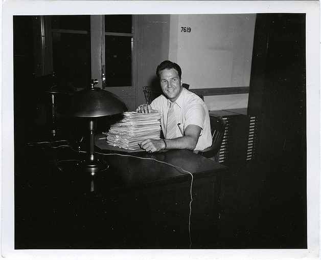 A man sitting at a desk with a stack of papers, paying back student loans.