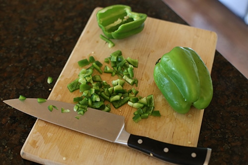 Chopping green pepper on wooden cutting board.