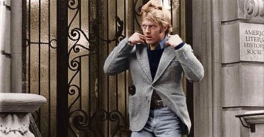 A man in a sports jacket and jeans is walking down the street.