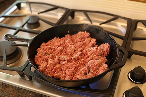Cooking frying sausage in cast iron skillet.