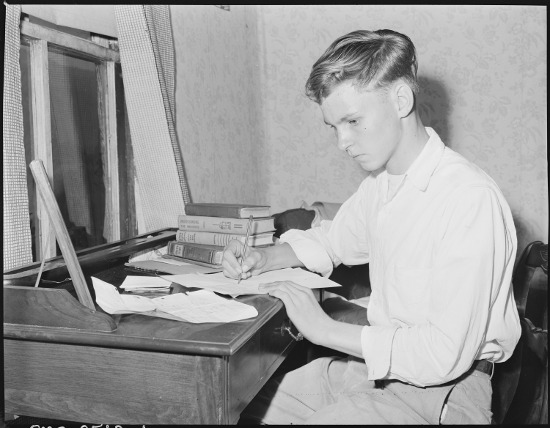 Young man writing essay on paper 1950s 1940s.