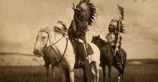 A black and white photo of a group of Sioux men on horses displaying physical toughness.