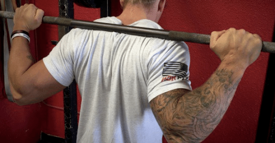 A man with tattoos is seen pumping iron in a gym.