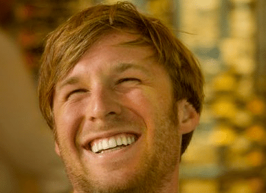 A man sits in a bar, smiling.