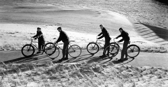 A group of men on bicycles enjoying a cheap recreation activity on the beach.