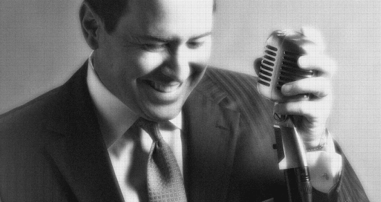 A black and white photo of a man in a suit holding a microphone, hinting at his potential singing career.
