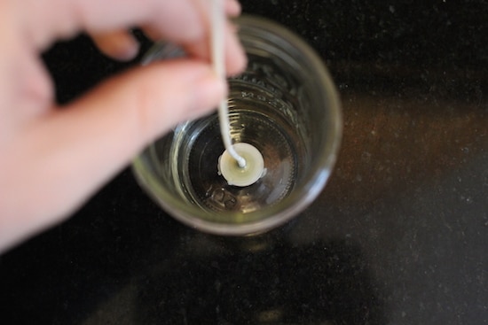 Adhering the wick to the container by hand.