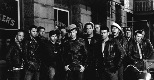 A group of men in leather jackets, exuding a rebel cool vibe, standing in front of a building.