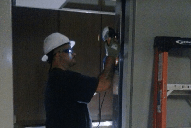An elevator mechanic in a hard hat working on a door.