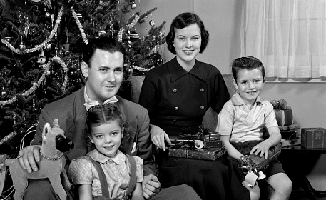 A black and white photo of a family posing in front of a Christmas tree with their kids.