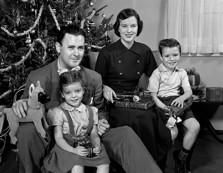 A black and white photo of a family posing in front of a Christmas tree with their kids.