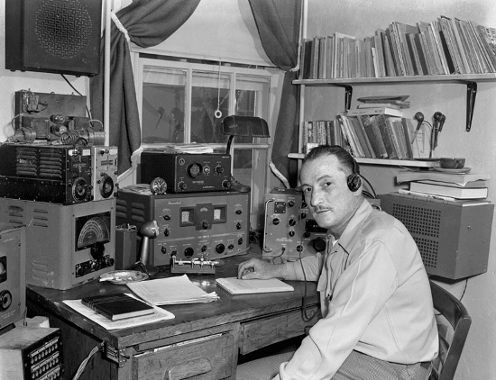 Vintage man at desk with ham amateur radio equipment.