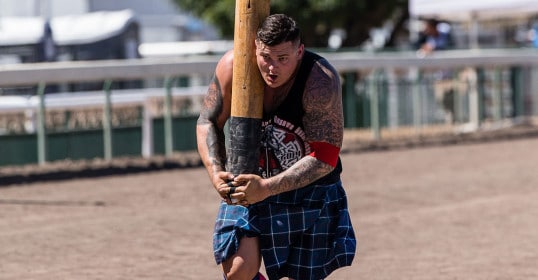 A man in a kilt training with a large wooden bat for the Scottish Highland Games.