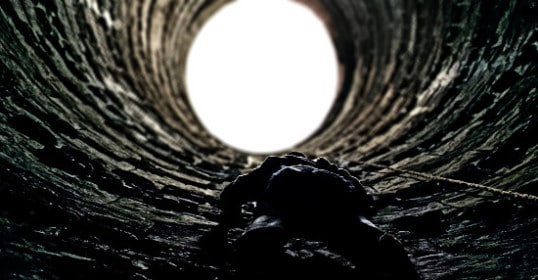 In a dark tunnel, a man shines his flashlight while climbing.