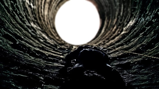 Man climbing out of pit well.